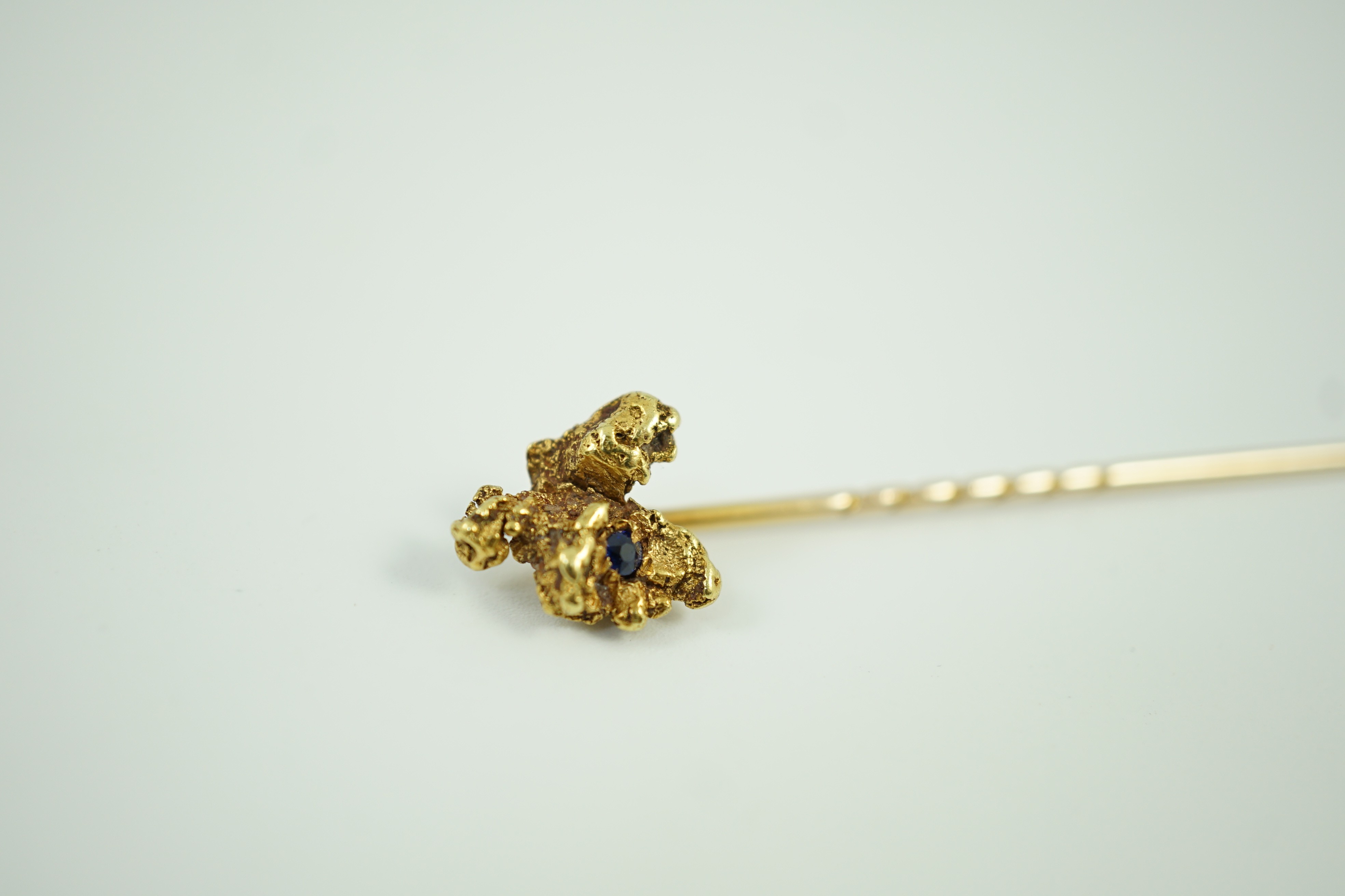 A late Victorian yellow metal and single stone sapphire set 'nugget' stick pin, 62mm, gross weight 3.2 grams.